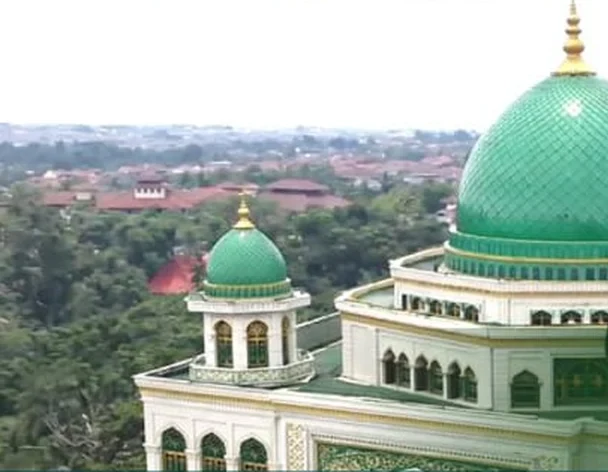 Foto masjid berkubah hijau dengan menara dan pepohonan di sekitarnya